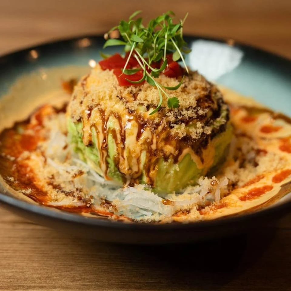 Niko Niko Sushi's avocado mountain, topped with microgreens, red peppers, sauce, and crunchy flakes.