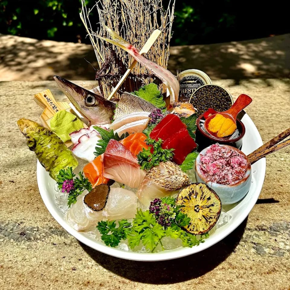 A large platter of assorted sashimi, including fish heads, caviar, uni, and wasabi, on ice.