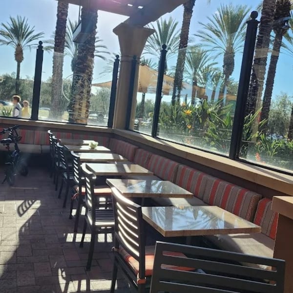Outdoor patio seating at Niko Niko Sushi with tables, chairs, and palm trees visible through large windows.