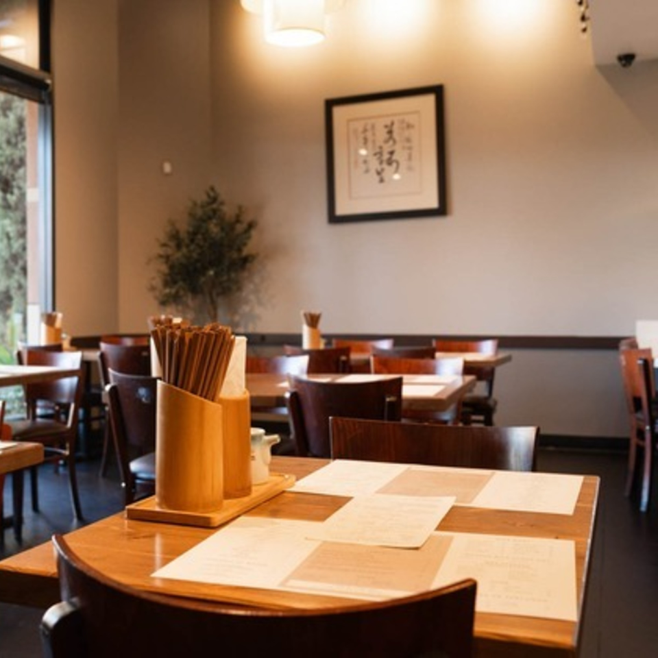 Interior of Niko Niko Sushi restaurant with wooden tables, chairs, and chopsticks on tables.